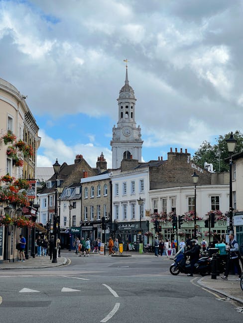 The image depicts a bustling street scene in Brunswick, featuring a cluster of charming Victorian and Georgian-style shops with flower boxes overflowing with colorful blooms. In the background, a prom